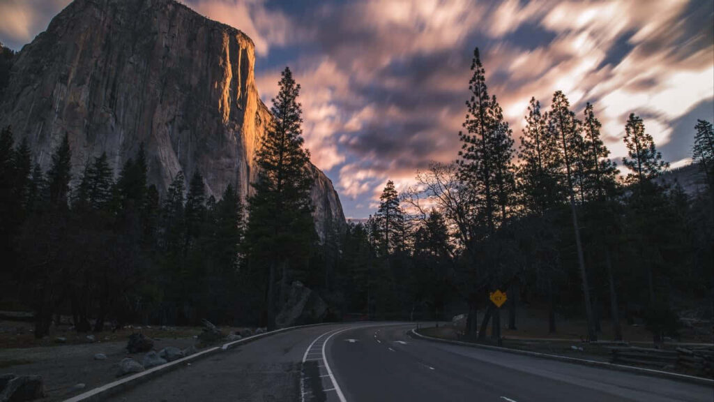 HD Wallpaper: Stunning Forest Road at Dusk - Cliffs, Trees, and Sunset Sky Background