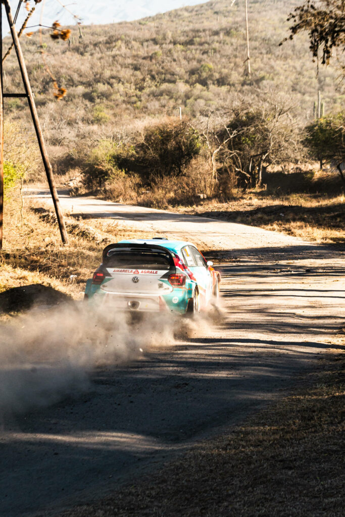 High-Octane Dirt Rally Race: Rally Car Dramatically Kicking Up Dust on Rural Road - Rally Racing Spirit Wallpaper