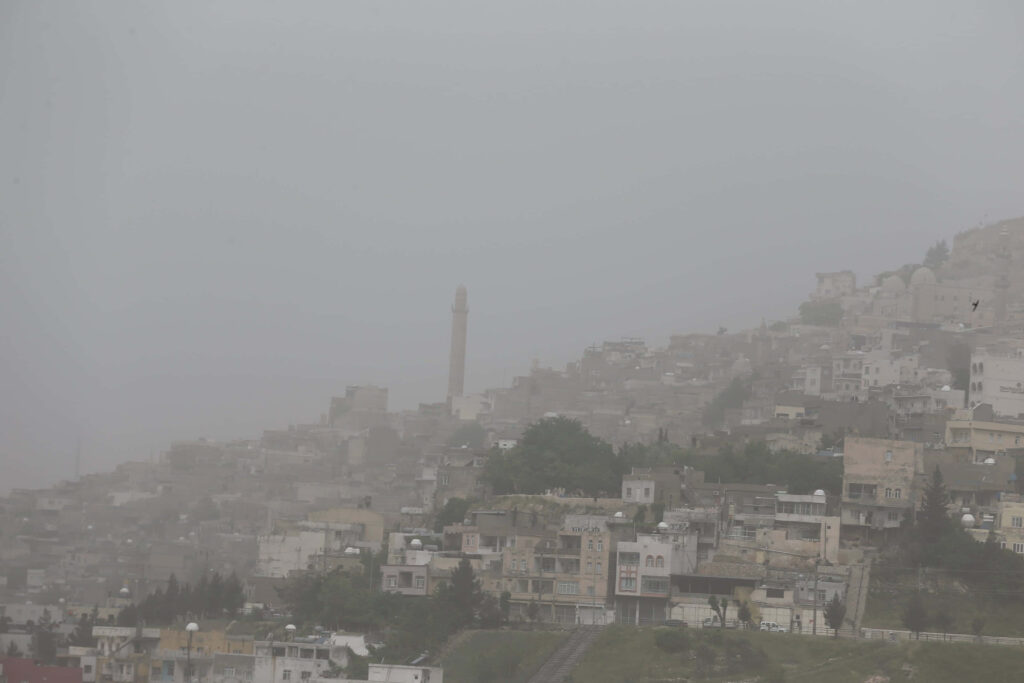 Dense dust storm envelops hillside cityscape with stone buildings and tall minaret in muted tones Wallpaper