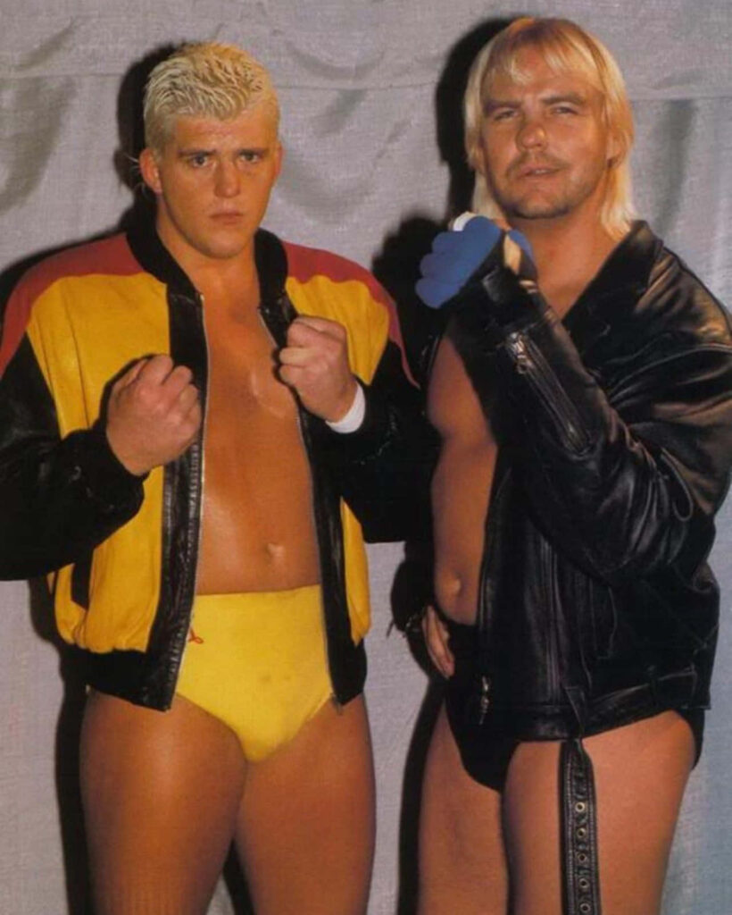 Dustin Rhodes and Barry Windham in wrestling gear posing confidently with wrestling wallpaper background