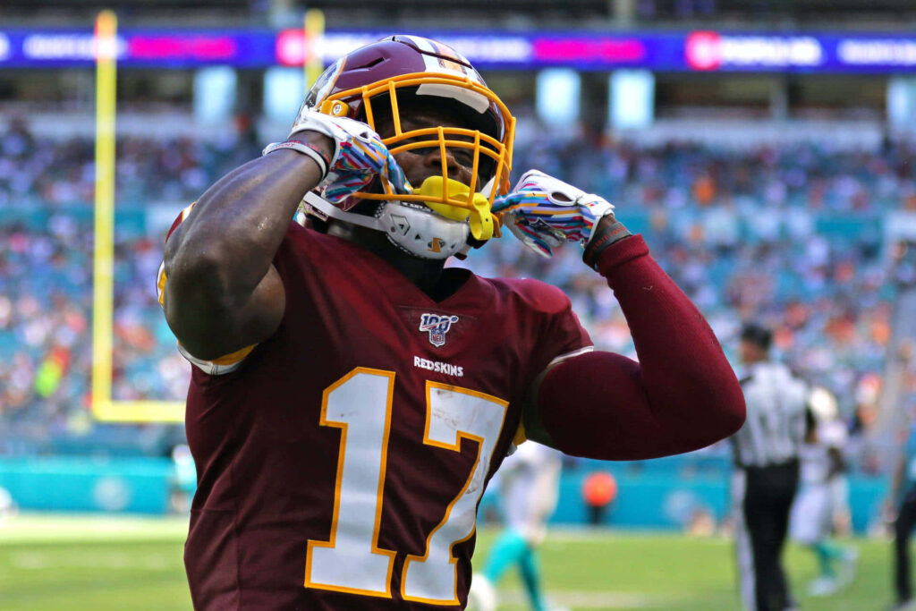 Dwayne Haskins in Washington Redskins uniform holding helmet on vibrant NFL stadium field background Wallpaper
