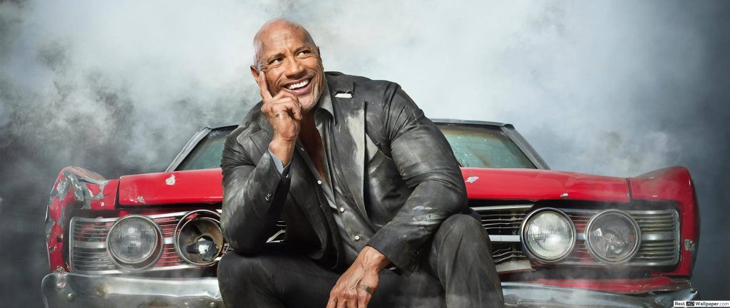 Dwayne Johnson as Luke Hobbs smirks on red muscle car in smoky gritty Fast and Furious wallpaper
