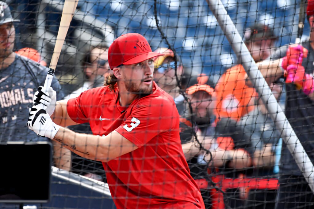 Dylan Crews in red jersey focused batting stance gripping bat before game with blurred crowd background Wallpaper