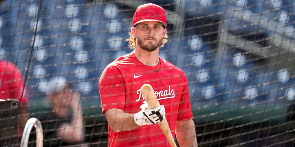 Dylan Crews focused in red Nationals uniform practicing batting in sunlit professional cage Wallpaper
