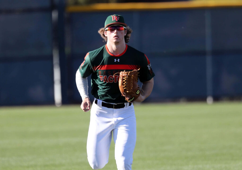 Dylan Crews mid-action baseball player in green black uniform on grass field daytime game Wallpaper