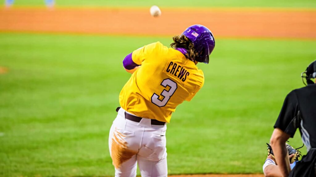 Dylan Crews mid-swing in yellow jersey number 3 purple helmet vibrant baseball field wallpaper background