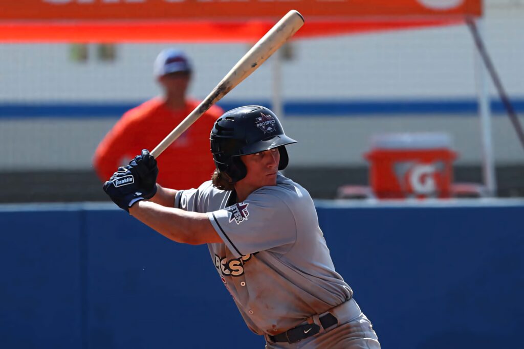 Dylan Crews mid-swing at bat wearing gray uniform and helmet during intense baseball game outdoors Wallpaper