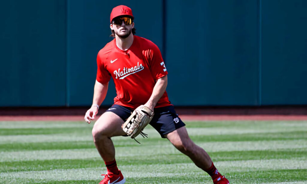 Dylan Crews fielding practice Nationals red jersey sunglasses on sunny green baseball field Wallpaper