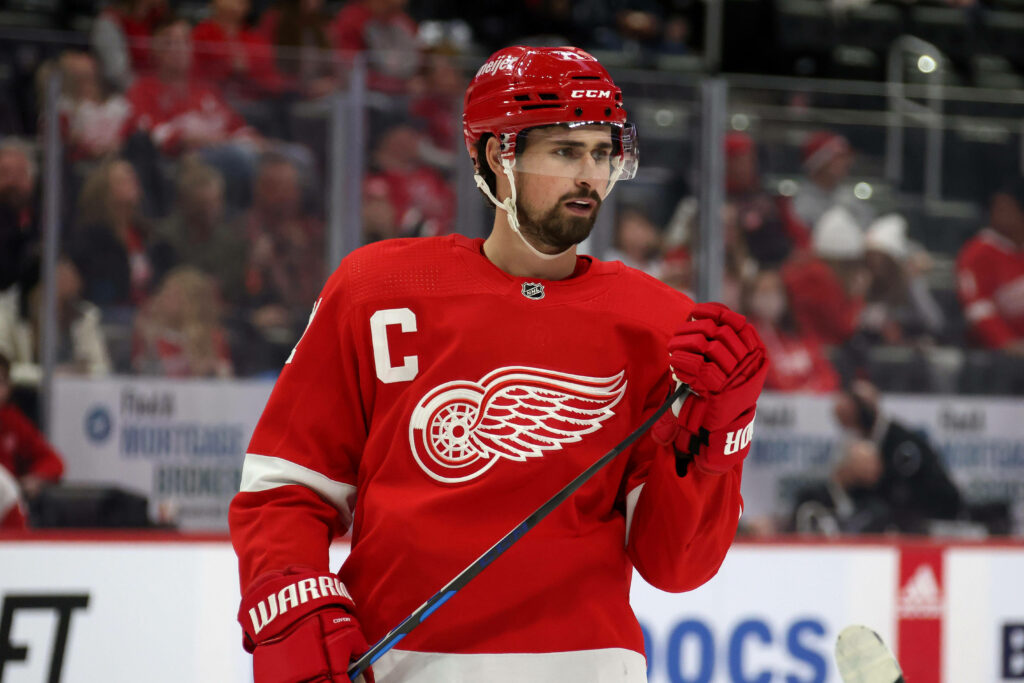 Dylan Larkin in red Detroit Red Wings jersey with captain C on ice intense hockey arena background Wallpaper