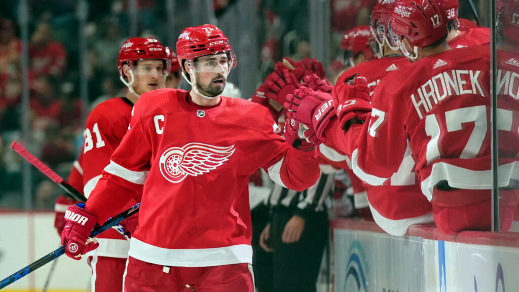 NHL player Dylan Larkin celebrates with Detroit Red Wings teammates in vibrant red hockey uniforms Wallpaper