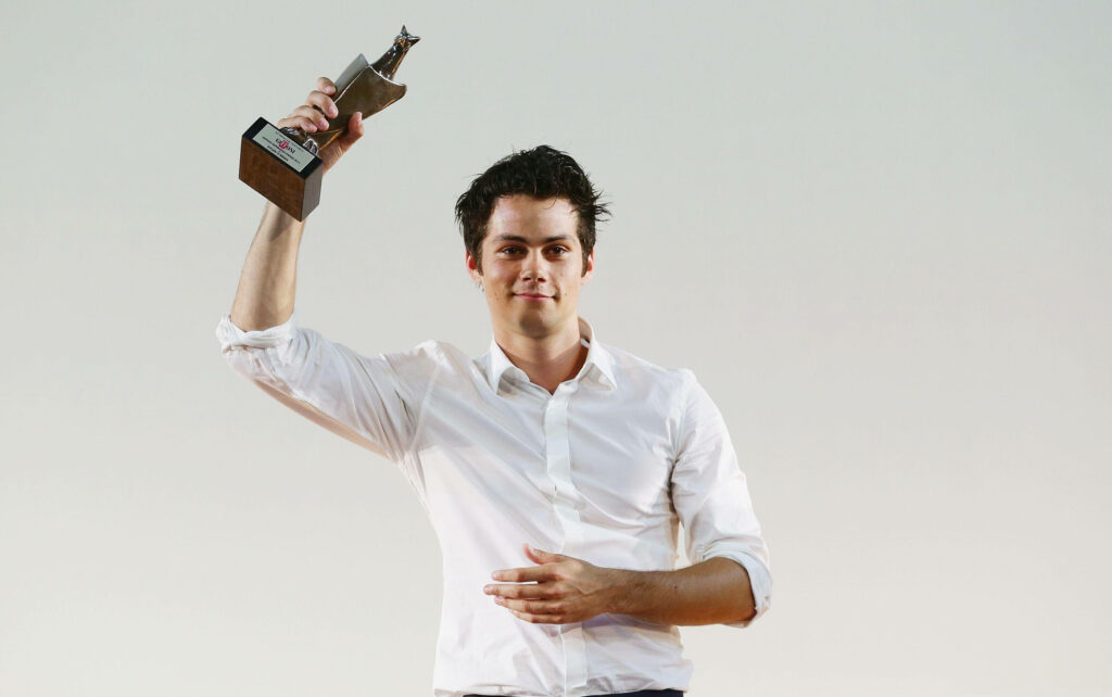 Dylan O'Brien holding award trophy in white shirt against plain background celebration wallpaper