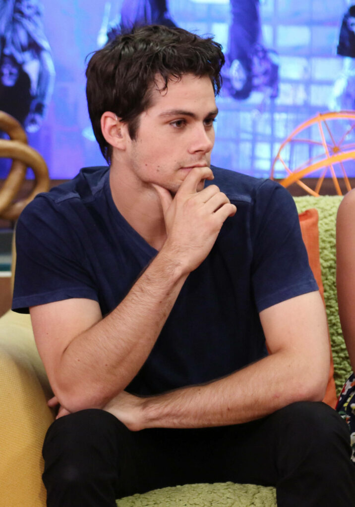 Dylan O'Brien in navy t-shirt and black jeans on colorful set during candid interview moment Wallpaper