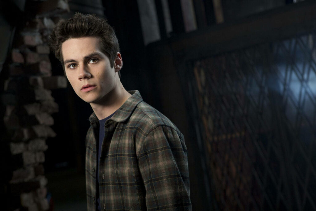 Dylan O'Brien in checkered shirt against moody industrial background with dramatic lighting Wallpaper