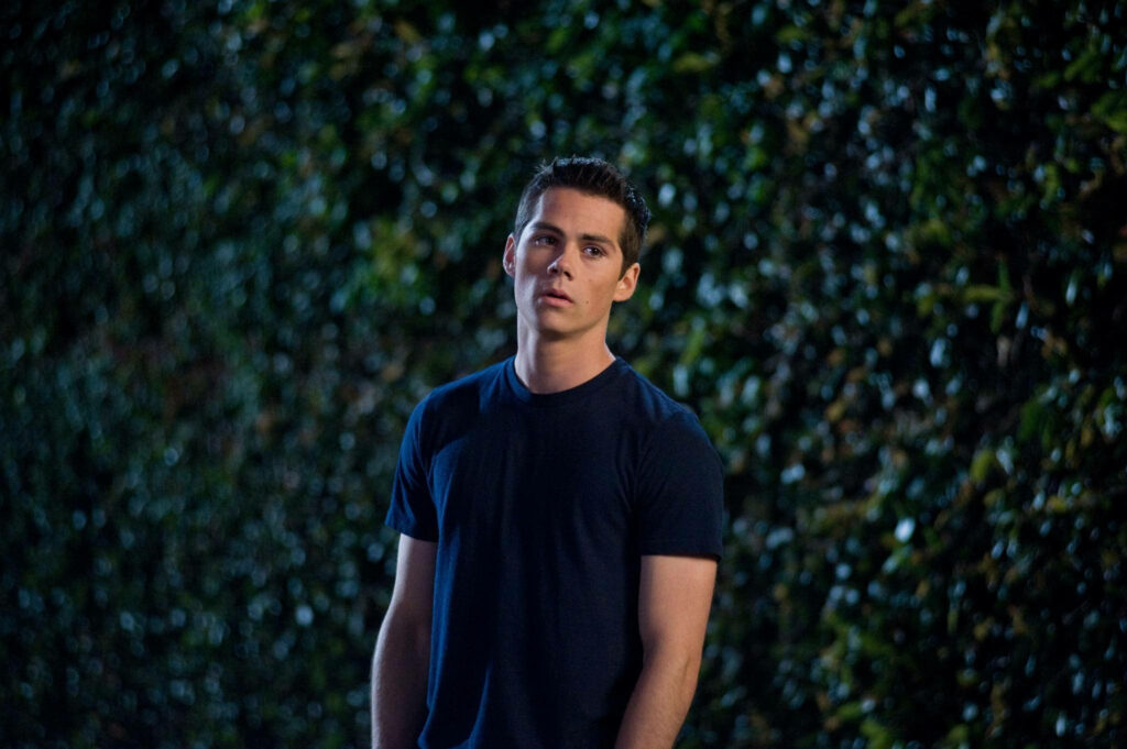 Dylan O'Brien in casual style under soft night light with lush green leaves background wallpaper