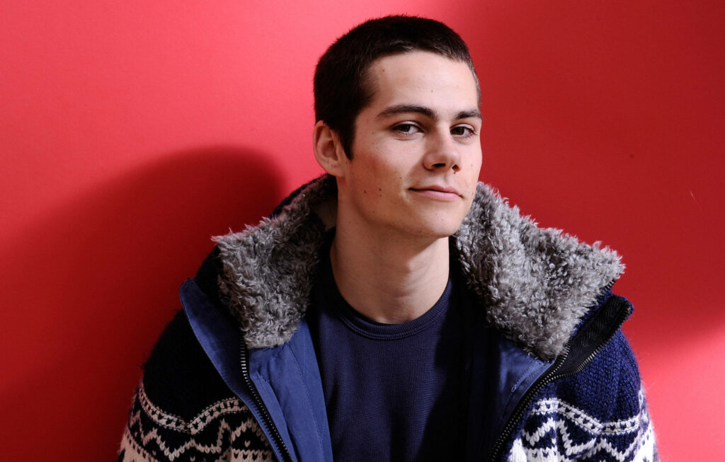 Dylan O'Brien in cozy sherpa jacket and navy shirt against bold red background with confident pose Wallpaper
