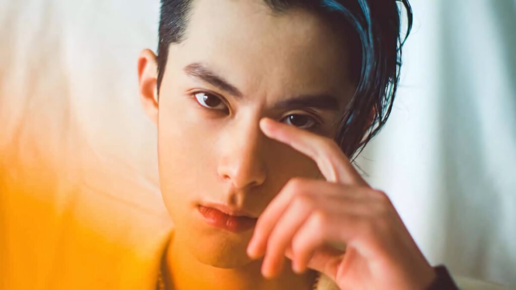 Close-up portrait of Dylan Wang with intense gaze and stylish hair on warm orange background wallpaper