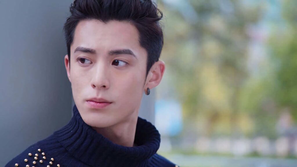 Dylan Wang looking left in navy studded sweater with soft blurred green background wallpaper