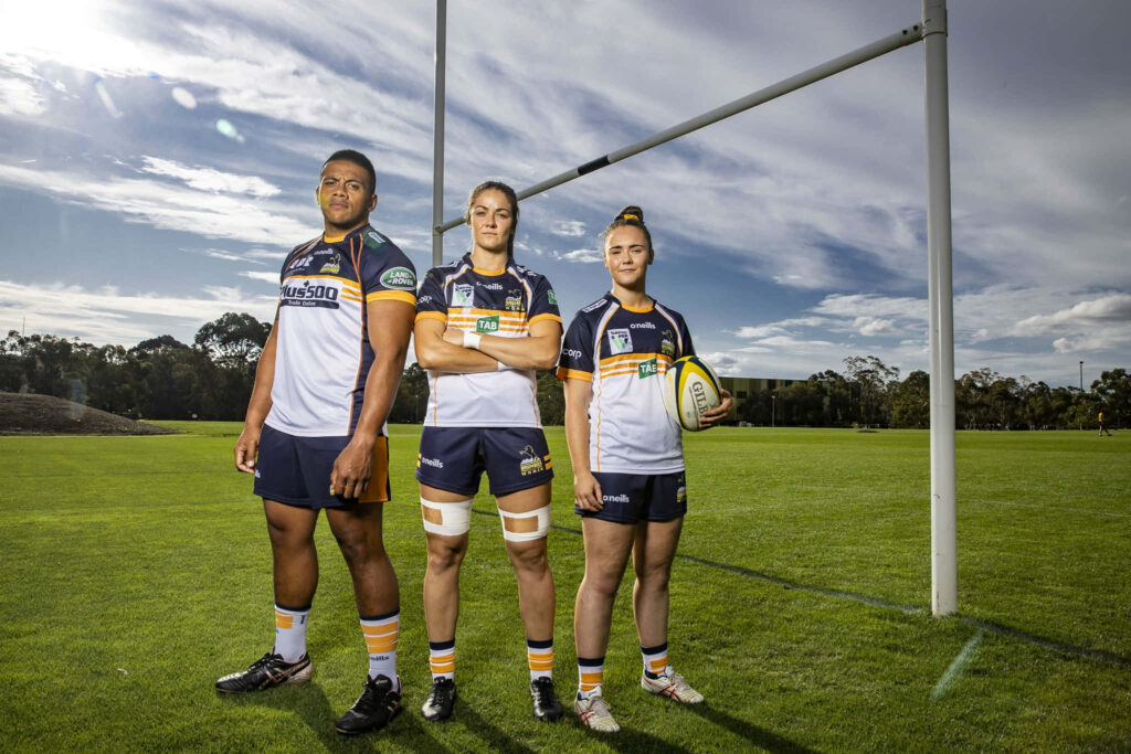 Dynamic ACT Brumbies rugby players in blue white gold uniforms posing on green field wallpaper