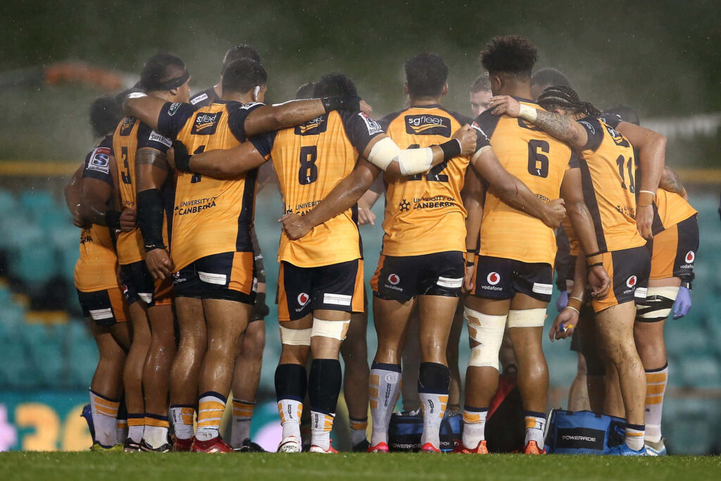 ACT Brumbies rugby team united in yellow and navy jerseys in wet stadium pre-game huddle Wallpaper