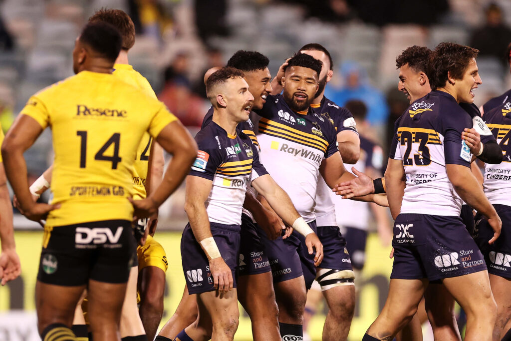 Dynamic ACT Brumbies rugby players celebrating in navy blue gold uniforms with stadium background Wallpaper