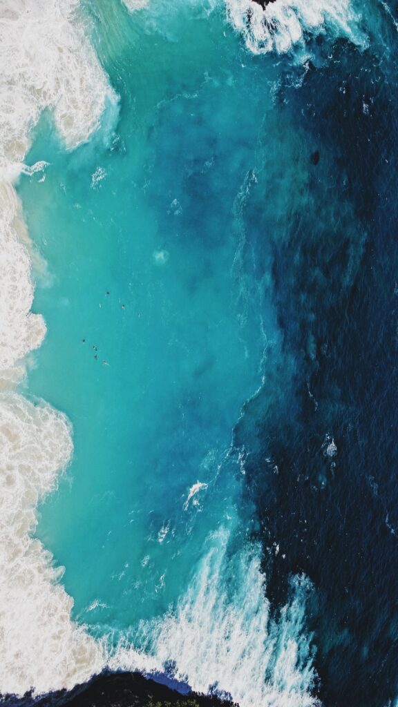 Aerial view of swirling ocean waves with white foam over vibrant deep blue water wallpaper background