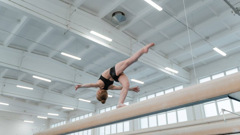 Female gymnast performing arch on balance beam in bright modern training gym environment Wallpaper