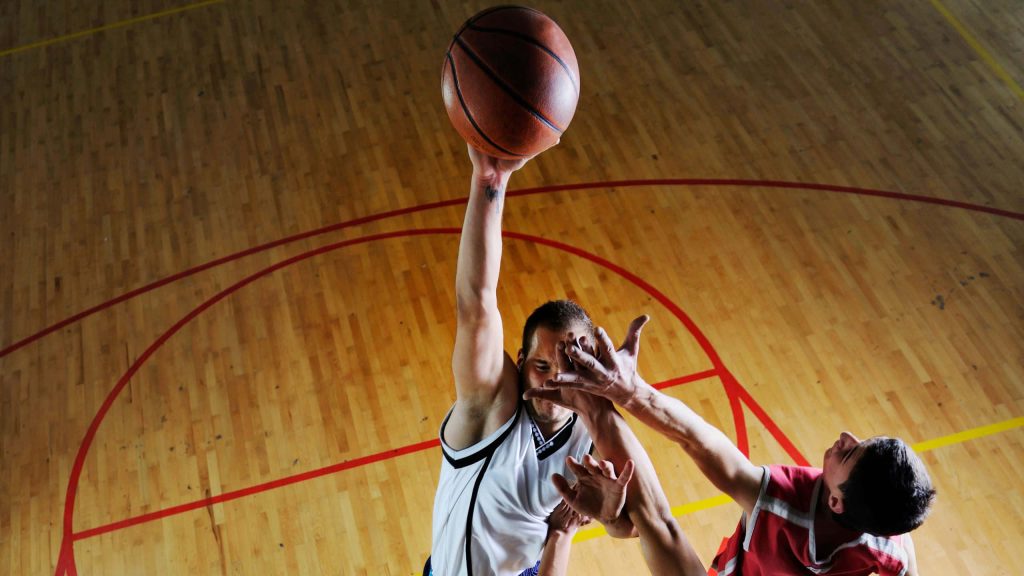 High-angle basketball dunk action with player in white jersey and defender in red jersey on court Wallpaper