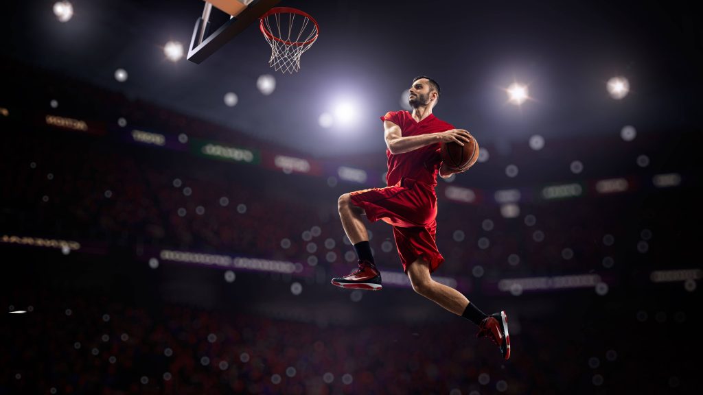 Basketball player in red jersey mid-air dunking in dim stadium with bright spotlights wallpaper