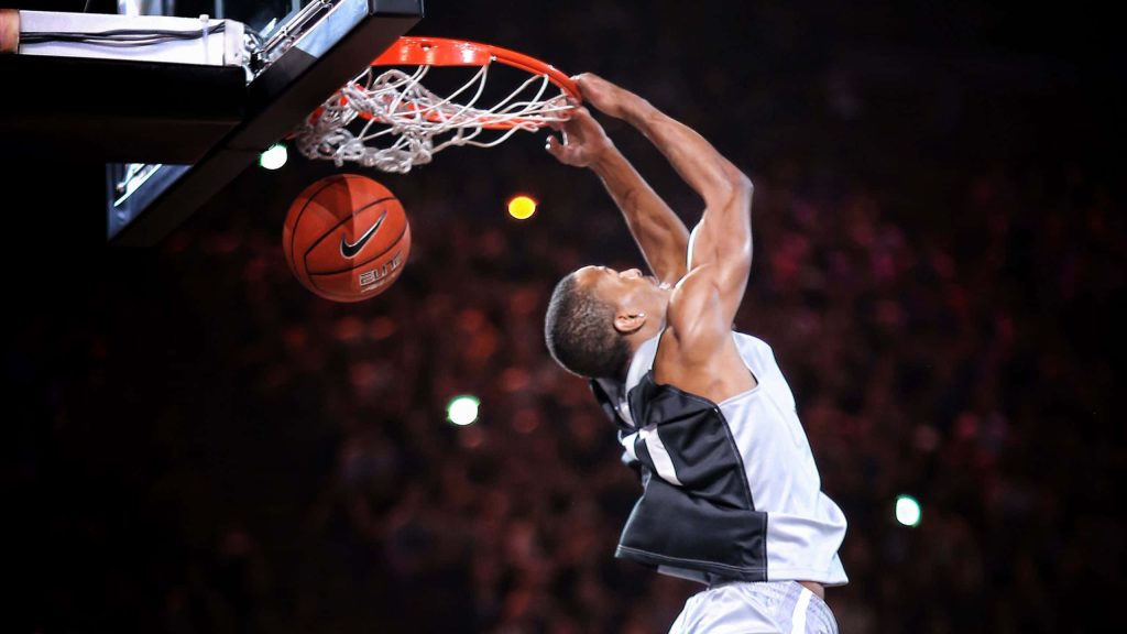 Pro basketball player slam dunk with Nike Elite ball in arena lighting and blurred crowd background Wallpaper