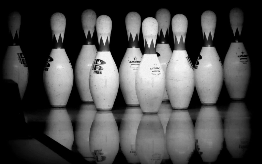 Dynamic black and white wallpaper of professional bowler striking pins on glossy lane with motion