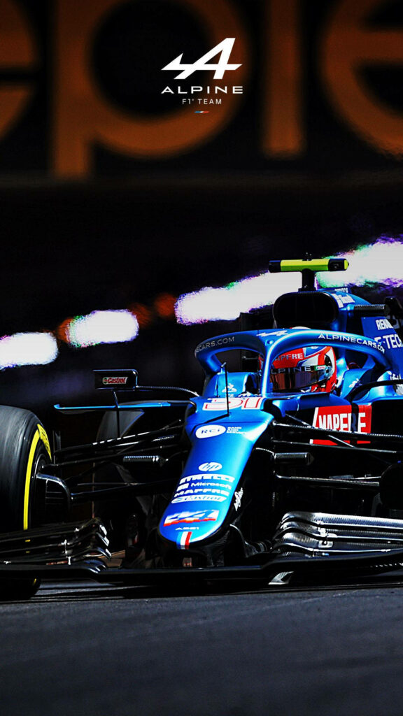 Blue Alpine F1 car racing under bright lights with Alpine F1 Team logo on wallpaper background
