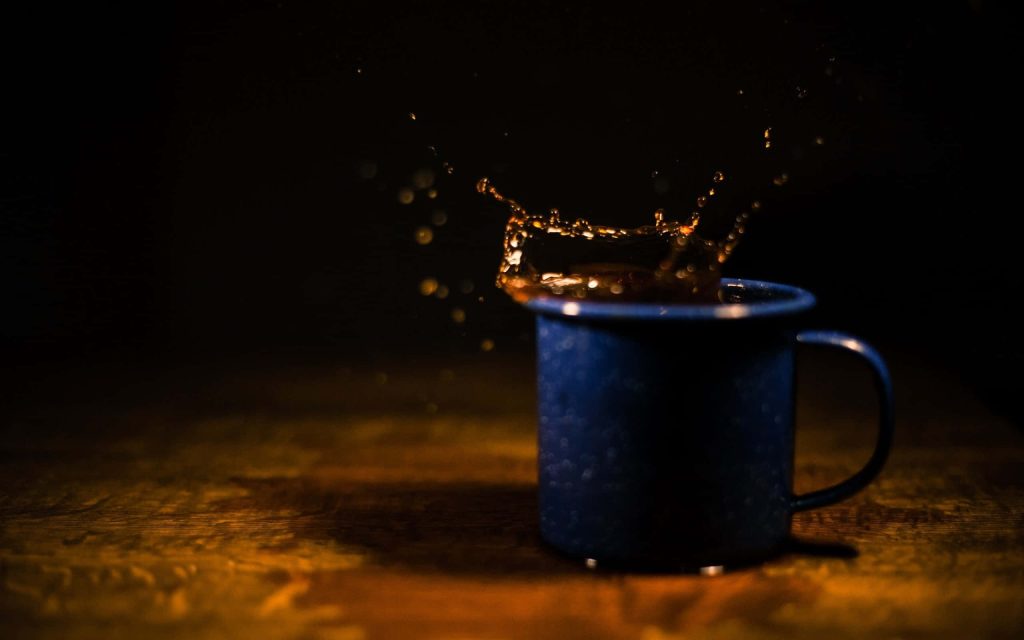 Dark enamel mug on rustic wood with vibrant blue liquid splash in dramatic lighting wallpaper