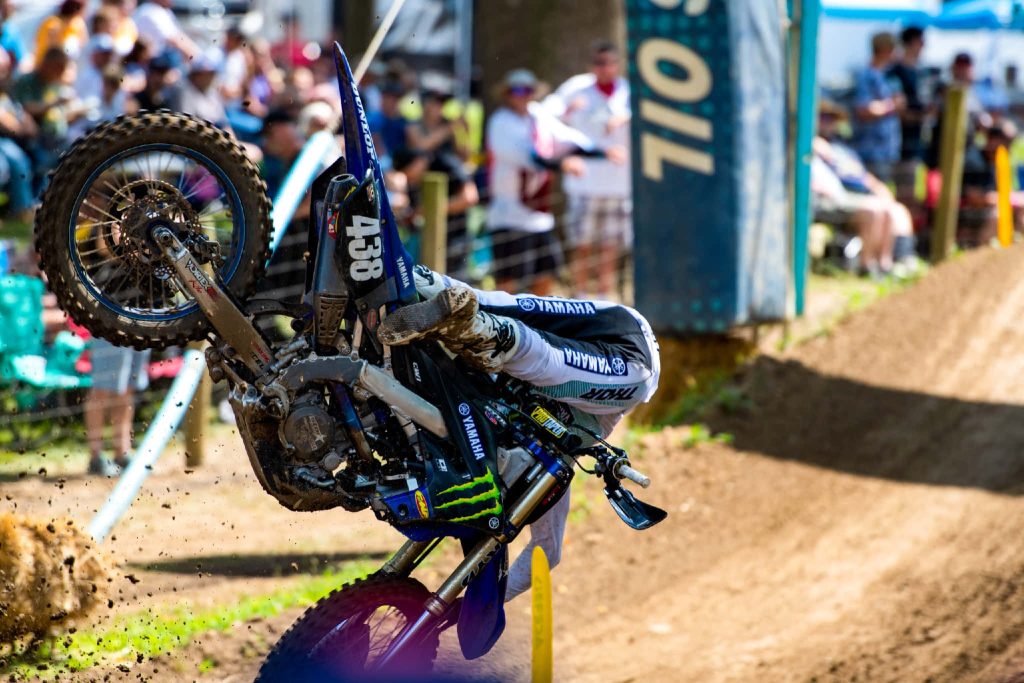 Blue Yamaha dirt bike mid-crash in dynamic motocross race with blurred crowd background Wallpaper