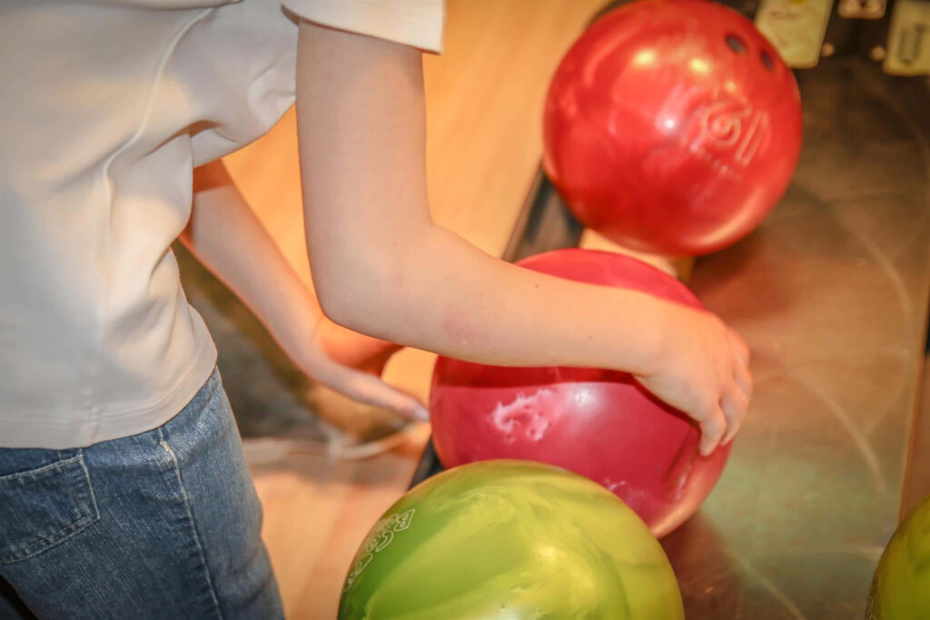 Bowler choosing vibrant red ball from colorful bowling lane rack in exciting sports action wallpaper