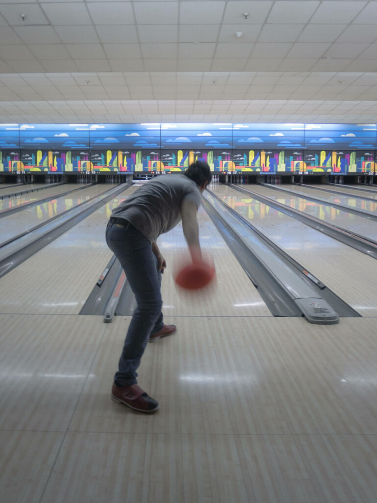 Person releasing bright red bowling ball mid-action on sleek lane in vibrant modern alley wallpaper