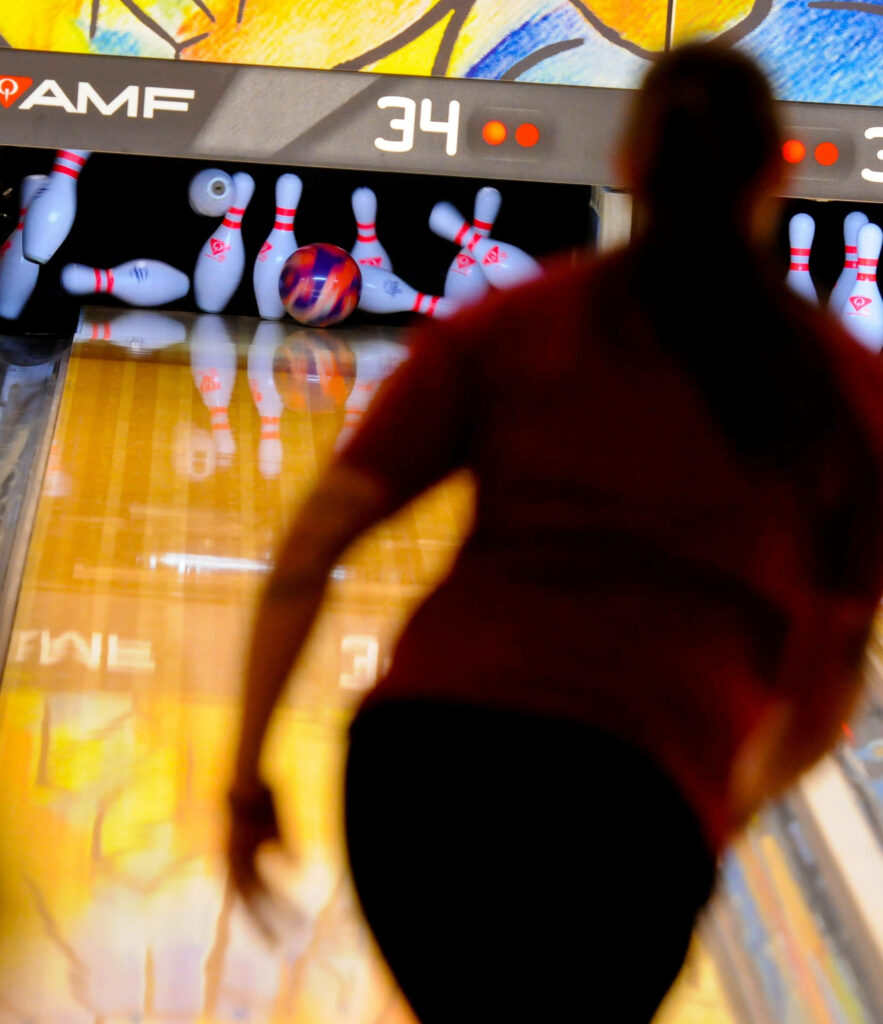 Silhouetted bowler releasing colorful ball at pins striking in vibrant bowling lane wallpaper