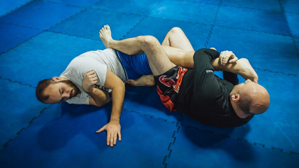 Dynamic BJJ Training: Athletes Practicing Leg Locks on Blue Mat Wallpaper