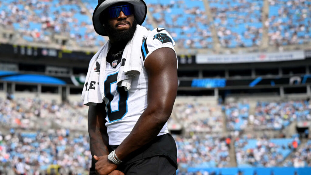 Brian Burns in Panthers jersey striking athletic pose stadium wallpaper bold team colors