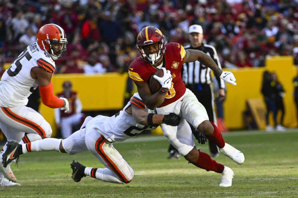 Brian Robinson Jr dodging tackle in red and gold uniform under bright stadium lights NFL action Wallpaper