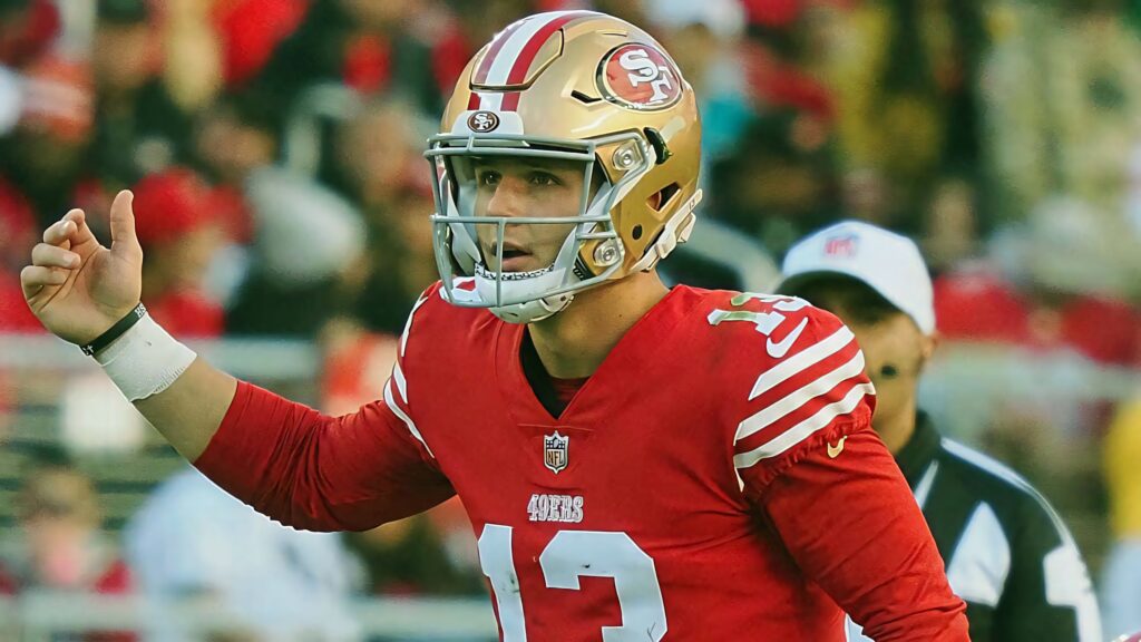 Brock Purdy 49ers quarterback in red uniform and gold helmet focused during NFL game action Wallpaper
