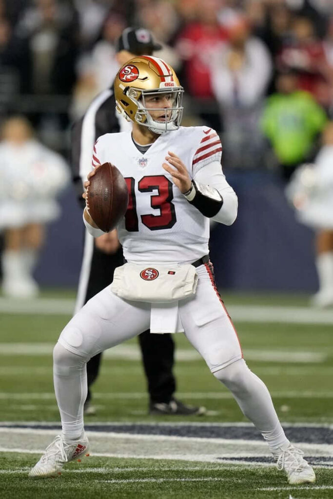 Brock Purdy 49ers quarterback in white red uniform poised to pass on football field wallpaper