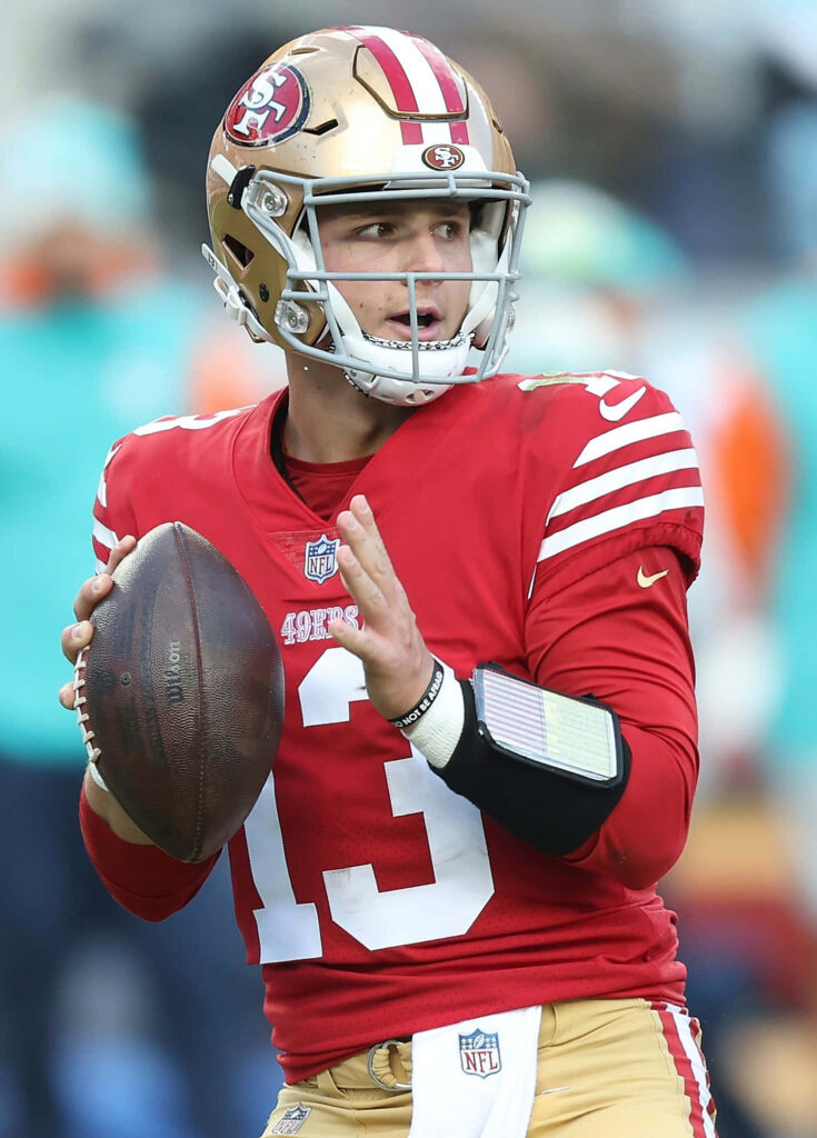 Brock Purdy 49ers quarterback in red gold uniform focused preparing to throw football action wallpaper