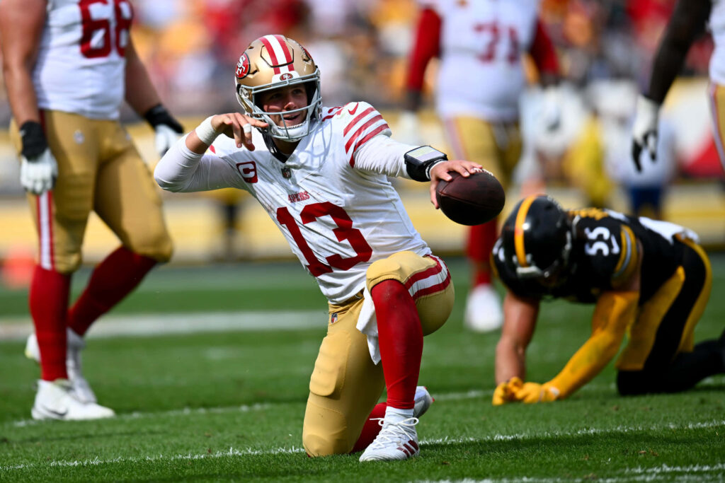 Brock Purdy dodging tackle vibrant San Francisco 49ers quarterback NFL action wallpaper background