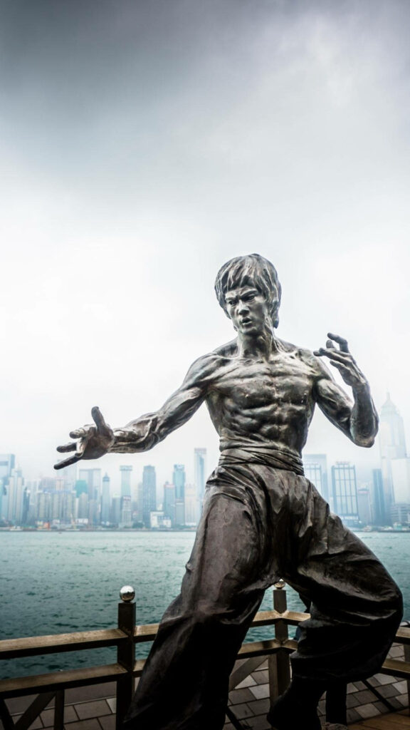 Bruce Lee statue in iconic fighting pose with misty Hong Kong skyline background wallpaper