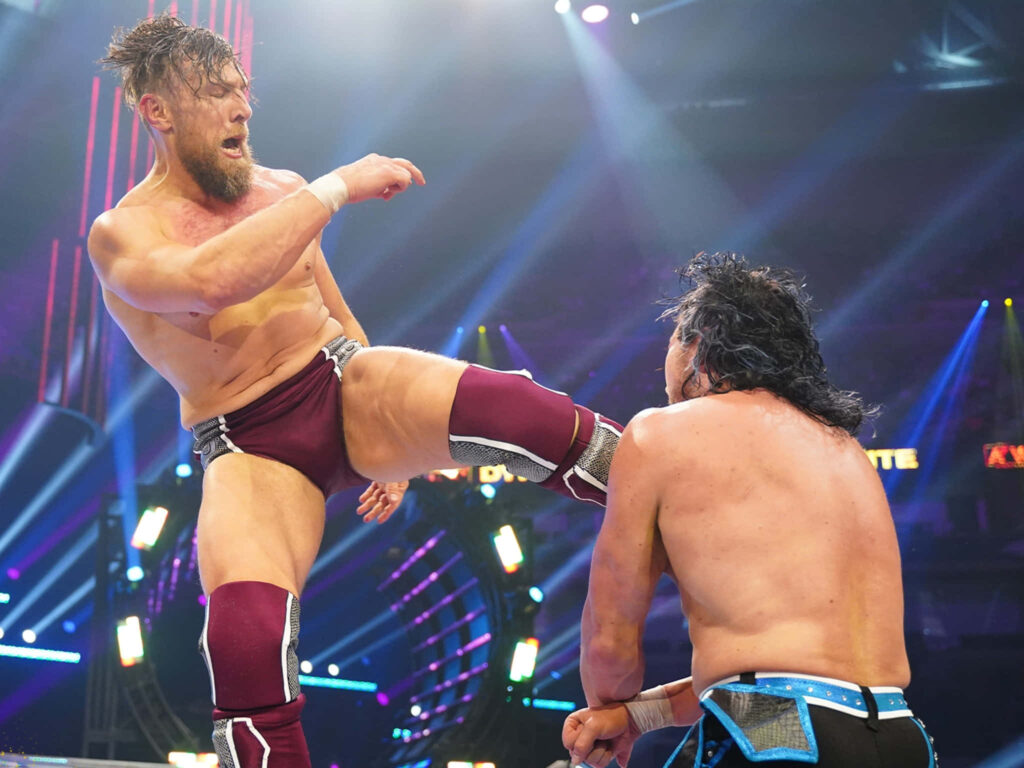 Bryan Danielson delivering powerful kick in maroon ring gear vibrant arena lights wrestling action Wallpaper