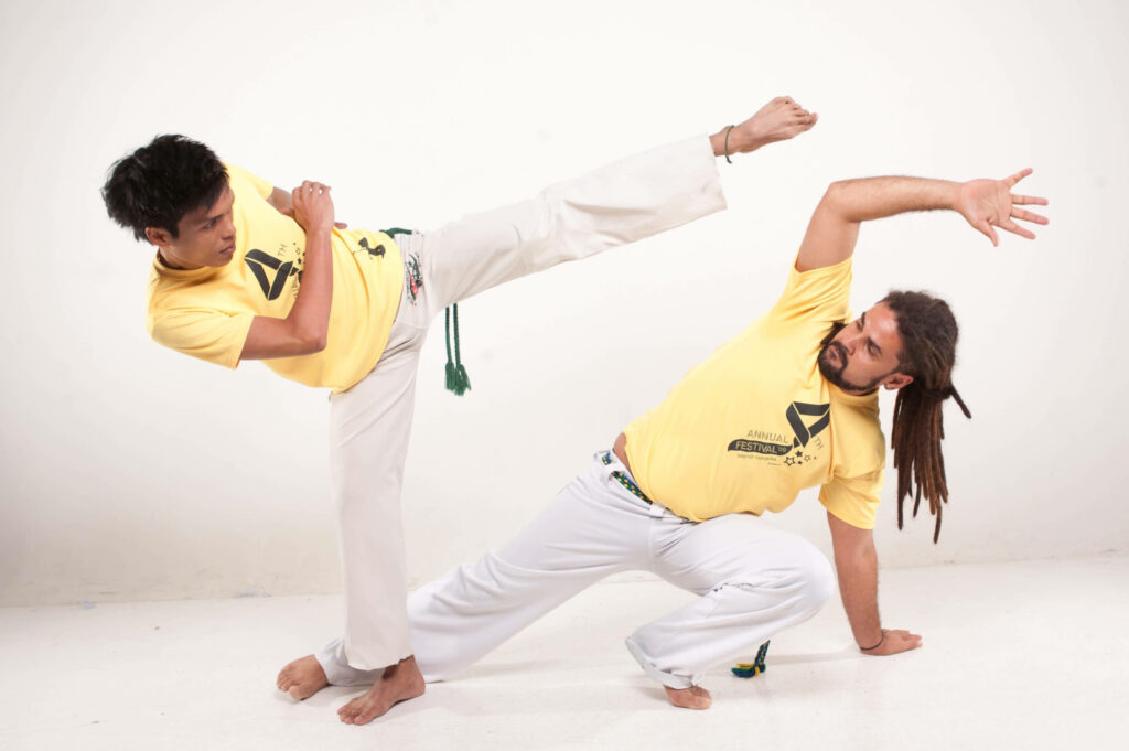 Two men in yellow shirts perform dynamic capoeira moves showcasing agility and balance on white background Wallpaper