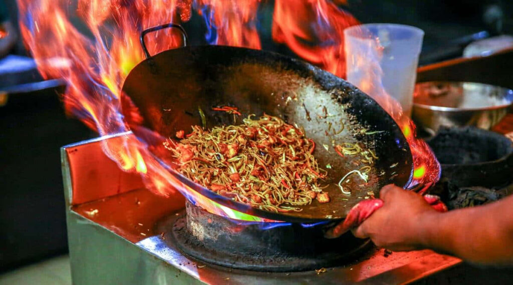Vibrant Chef Stir-Frying in Wok | Dynamic Cooking Scene Wallpaper