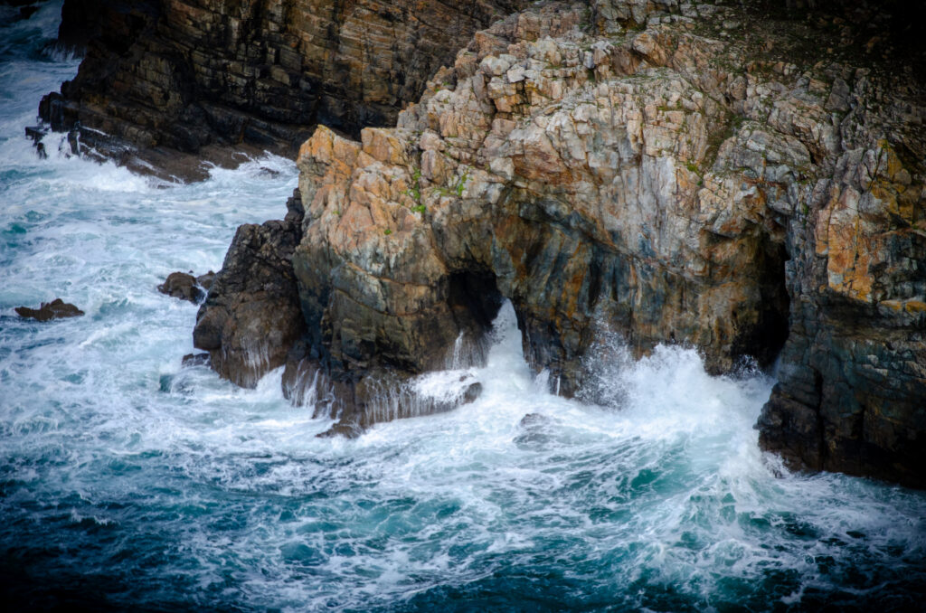 Vibrant sea waves crashing on rugged rocks near shadowy cave coastal wallpaper background