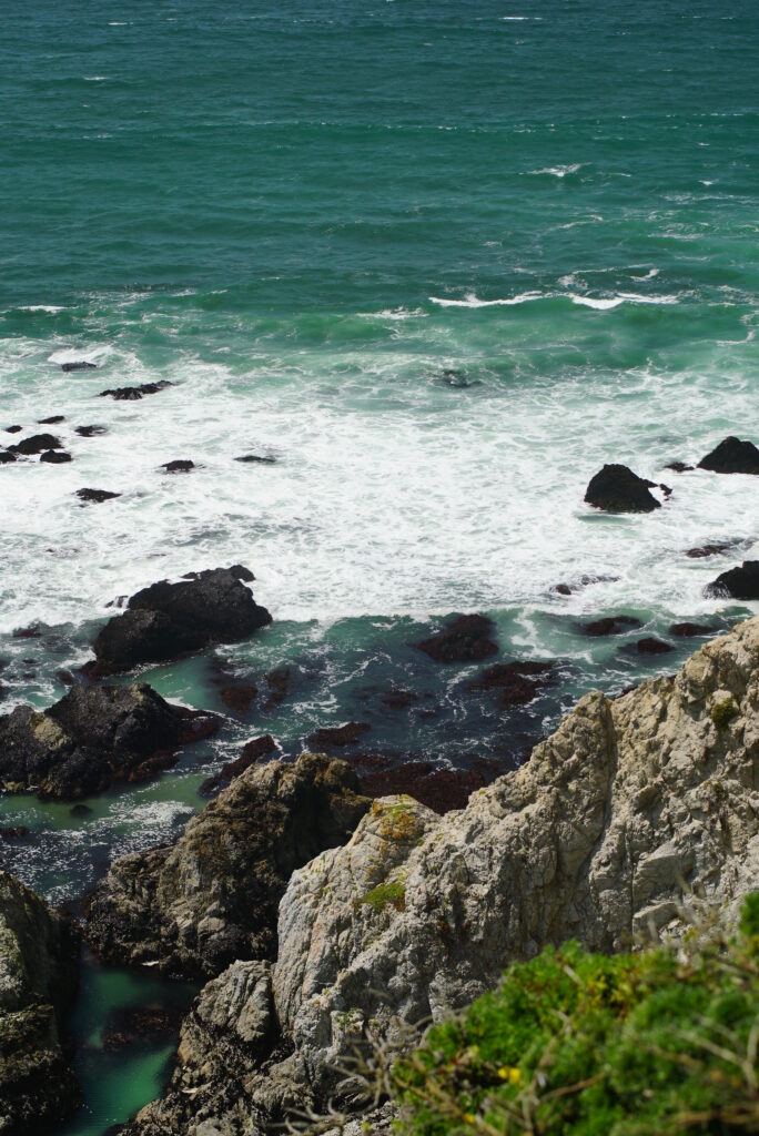Vibrant blue green ocean waves crashing on rugged coastal rocks with dynamic natural scenery wallpaper