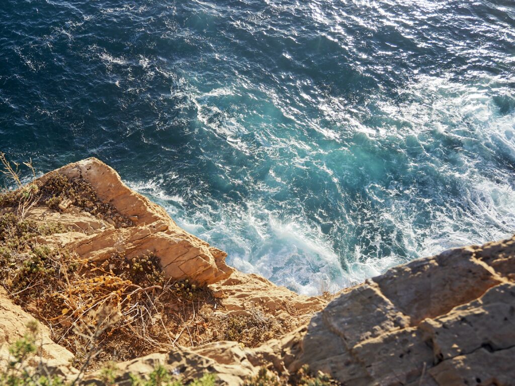 Dynamic coastal wallpaper with deep blue waves crashing white foam on sunlit rugged rocks